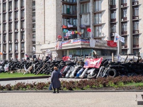 John E. Ramspott, Woman Looking at Pro-Russian Separatist Headquarters (Ukraine), printed on aluminum, 20 by 30 inches.