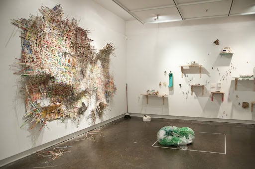 installation showing a woven cardboard grid, like a fraying blanket, situated on wall