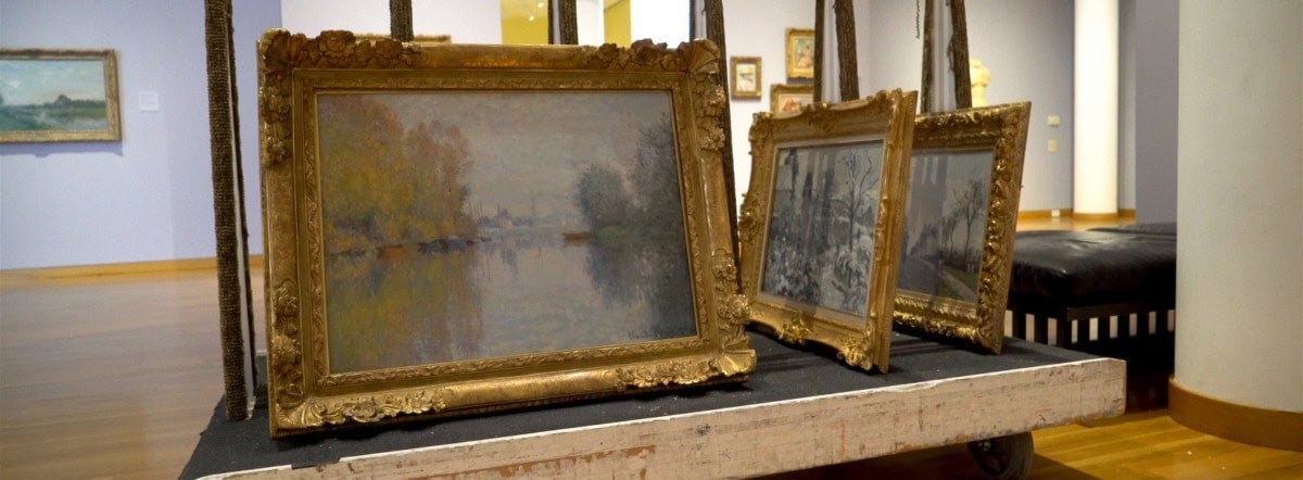 three landscape paintings in gold frames wait to be reinstalled