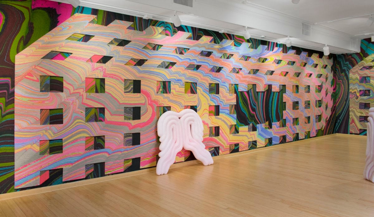 A curly white sculpture is tilted against a colorful gallery wall.
