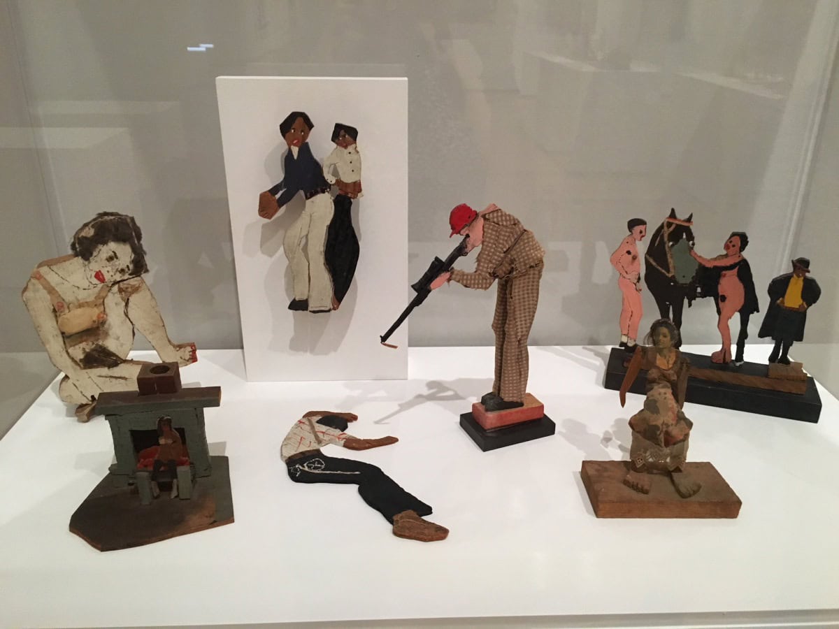 VItrine containing flat, cutout figures, including a white man pointing a rifle at a black man on the ground.