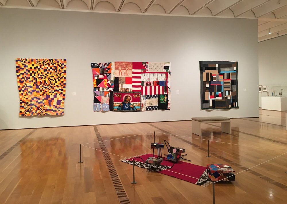 Installation view of "Outliers and AMerican Vanguard Art" at the High Museum, showing three Gees Bend quilts.
