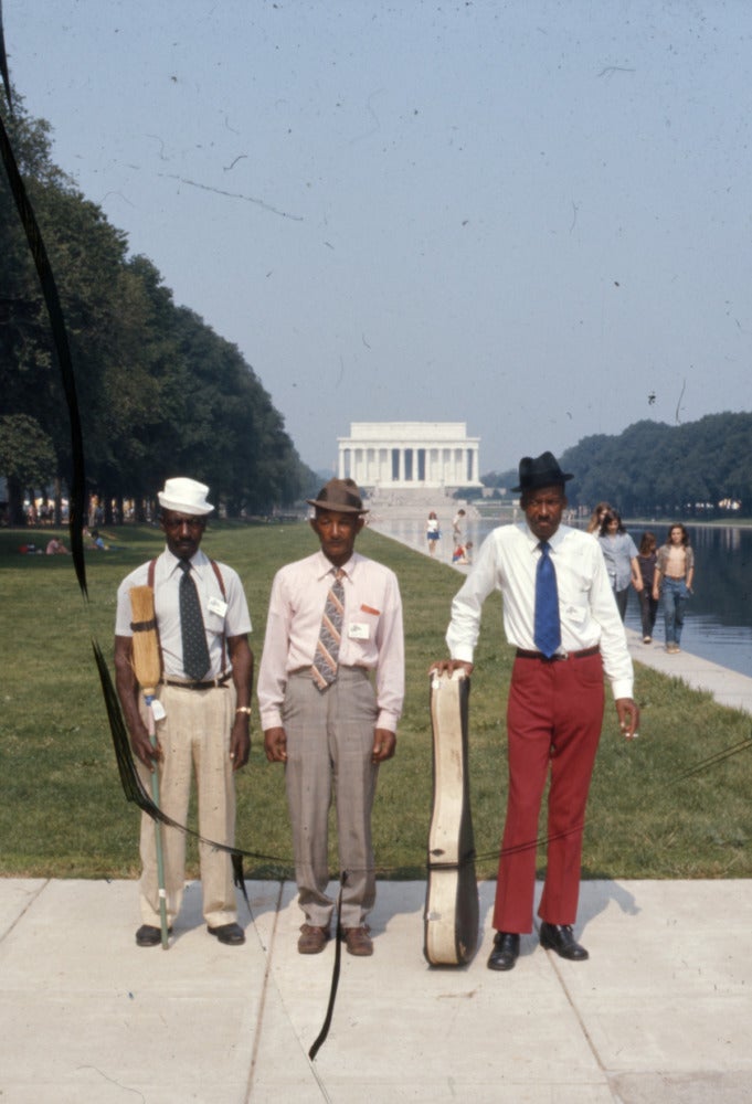 Three men stand in front of the Lincoln Memorial on the National Mall.
