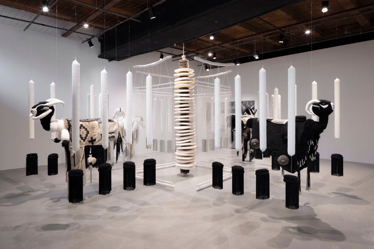 installation view of felt and wool sculptures of sheep hanging from the ceiling