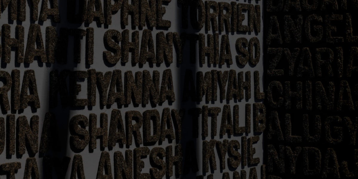 A wall displays the names of over 400 Black women and girls who have been reported missing and whose stories are largely unreported in the media. Their names are rendered in relief and constructed from black felt and discarded hair that appear to emerge from the jet black walls.