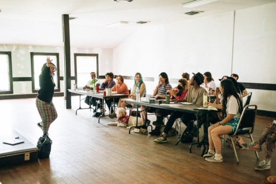 students in clusters gather to watch an instructor in motion in a bright classroom setting