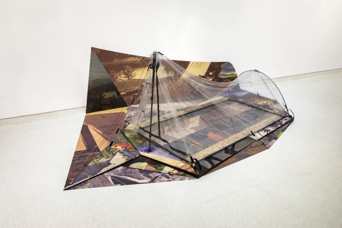 A clear plastic two-person tent on top of large scale images that mimic a shadow on the ground and wall.