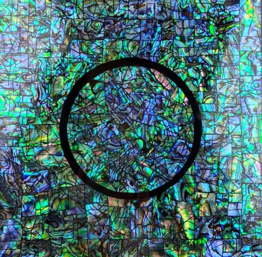a blue green iridescent surface with a black circle outlined in the center
