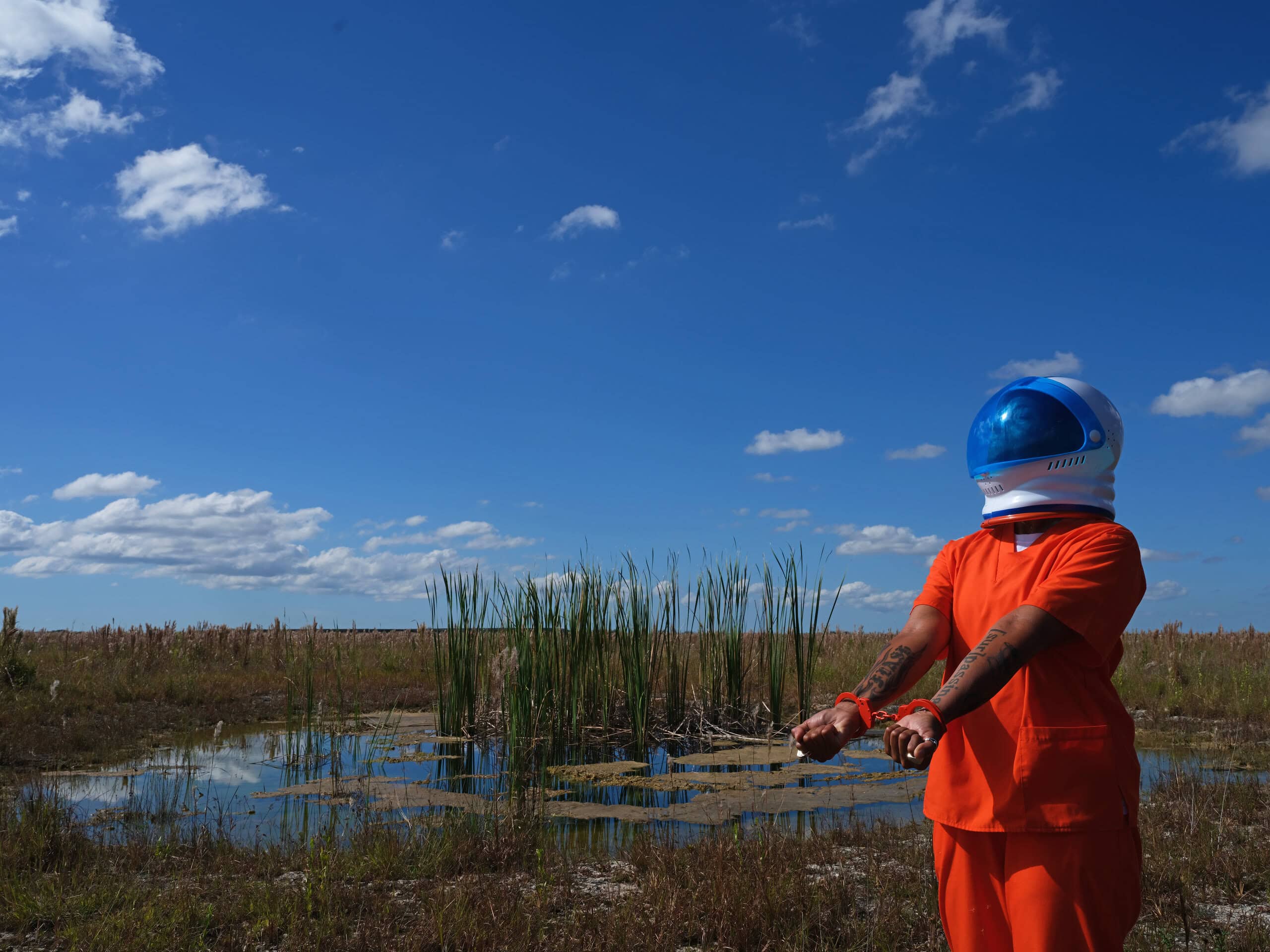 image of masked figure wearing a prison uniform in the Everglades